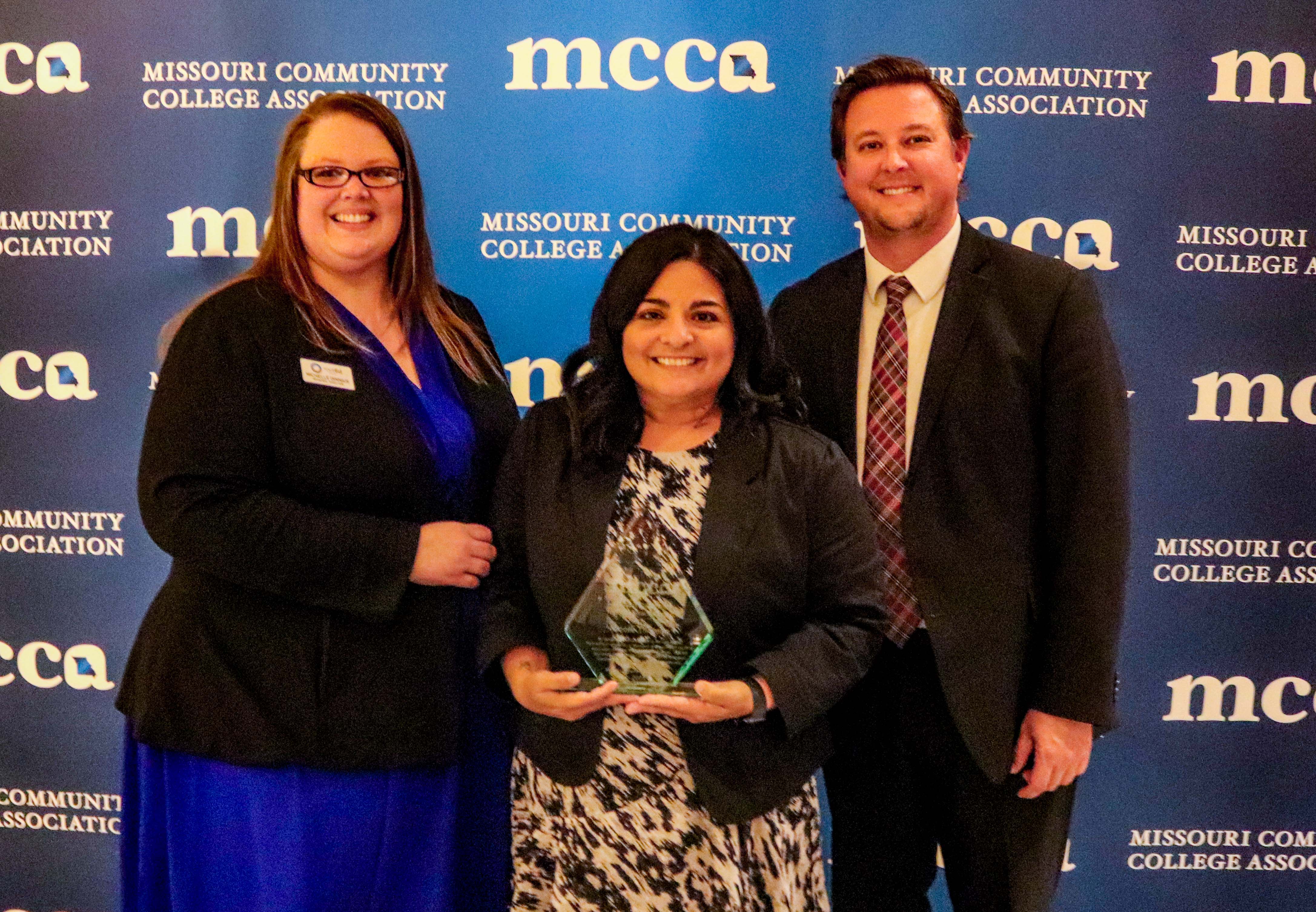 Photo of Michelle Dinnius, Nicole Thomas, and Dr. Joe Gilgour in front of MCCA backdrop