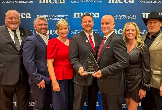 Kurt Bauche, Chris Hulsey, Camille Nations, Joe Gilgour, Bob Monks, Heather Monks, and Alan Wells in front of MCCA backdrop